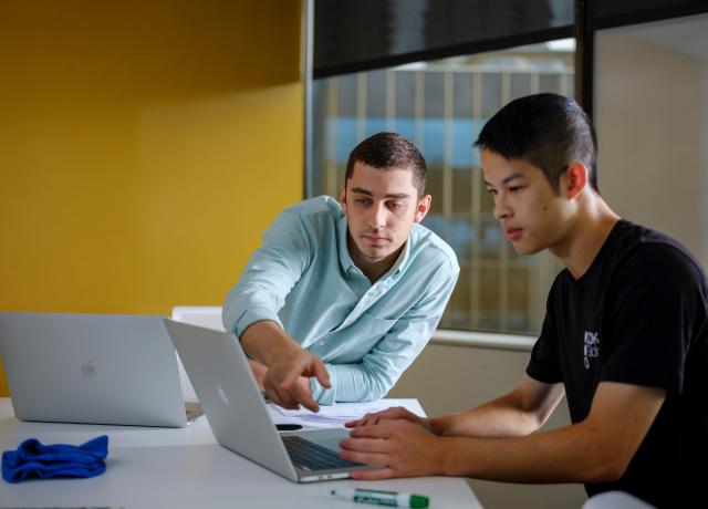 Two students seated at a table working together on a laptop.