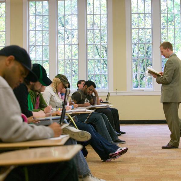Teacher in suit standing in front of seated row of students.