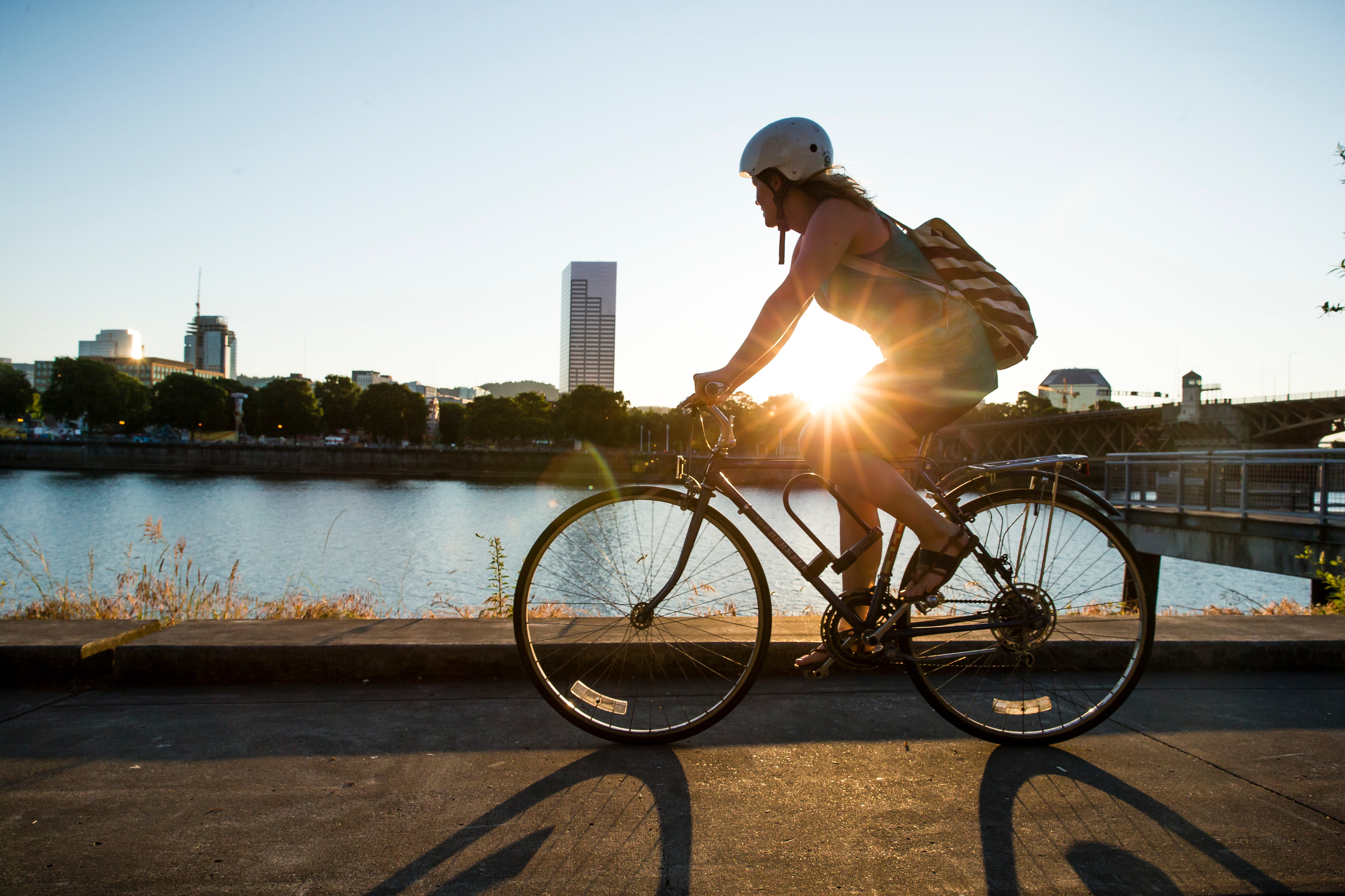 Person cycling by a river with the sun setting on the other side of them.