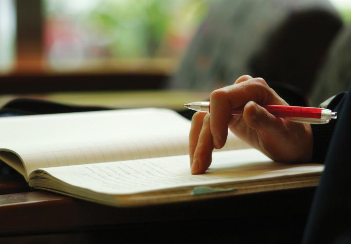 Hand holding a pen and resting on an open notebook.