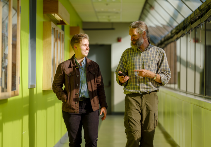 Student and professor walking down hallway in conversation