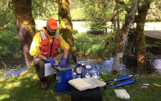 USGS hydrologist sitting by a body of water with a laptop and other scientific instruments