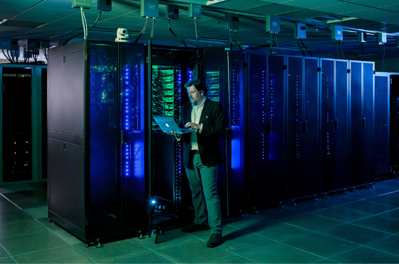 Man with laptop standing in front of supercomputer