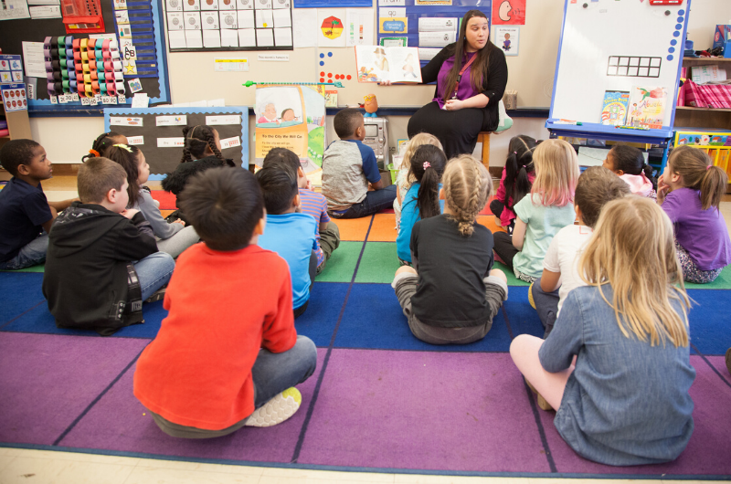 Teacher reading to young students seated on carpet