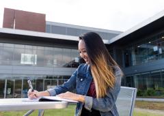 Woman seated at table outside, writing in notebook