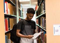 Man standing, reading opened book in library