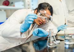 Woman with lab coat and goggles measures liquid into beaker