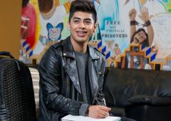 Man seated with notebook in lap and colorful mural in background