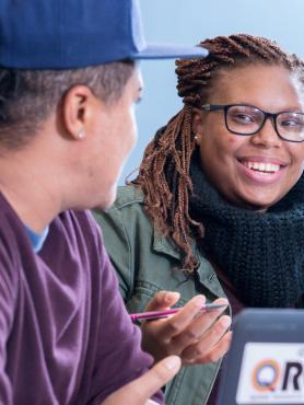Two students in conversation with a laptop in foreground