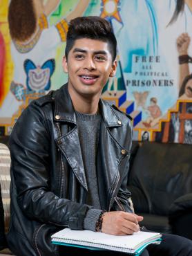 Man seated with notebook in lap and colorful mural in background