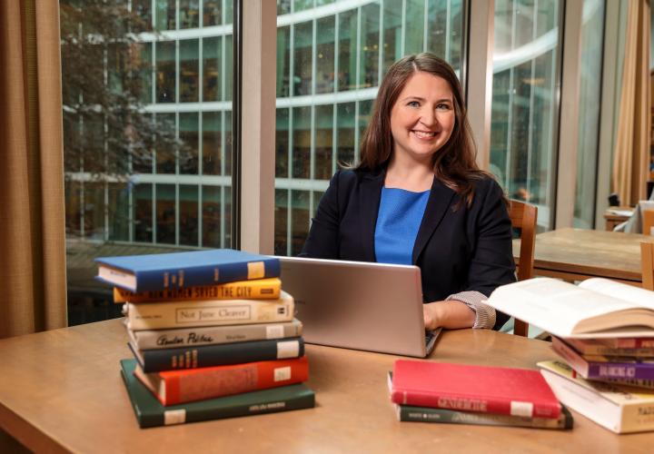 Professor with laptop and stacks of book on table in library