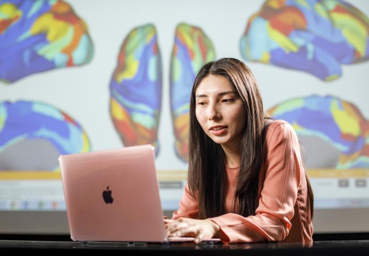Student typing on laptop with graphics of brain maps in the background