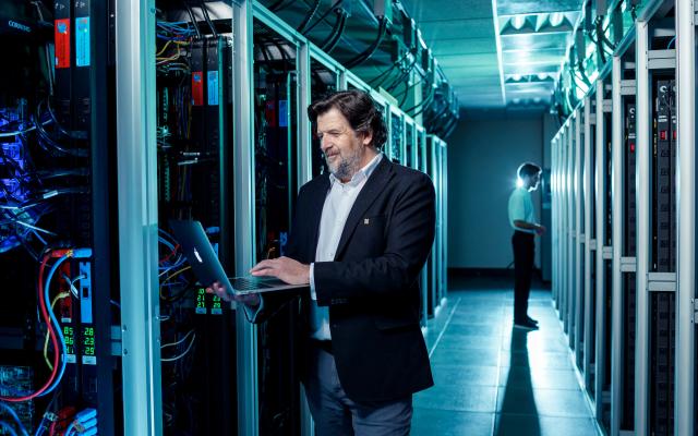 Man standing with laptop next to supercomputer