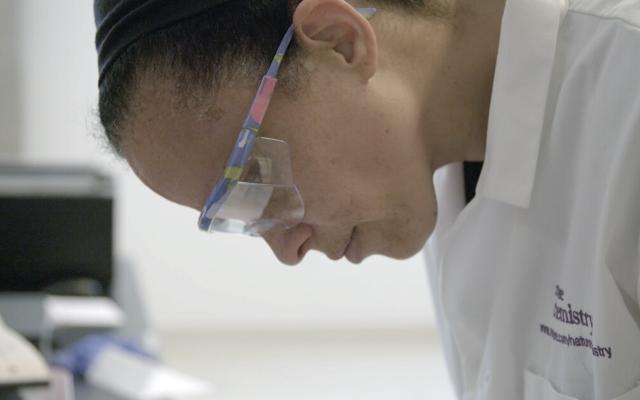 Scientist in lab coat and safety goggles looking down