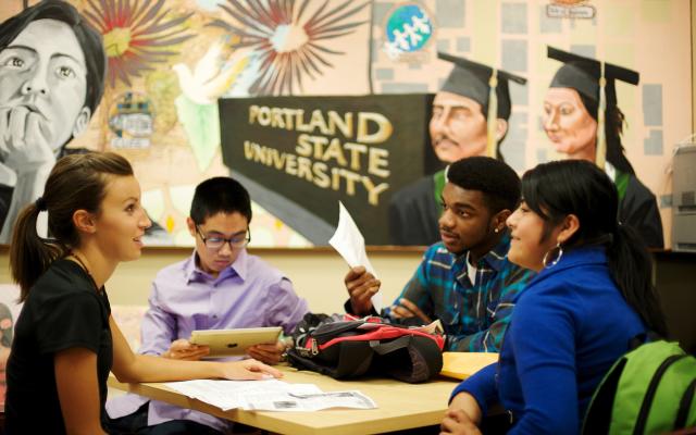 Four students around a table with a mural behind them