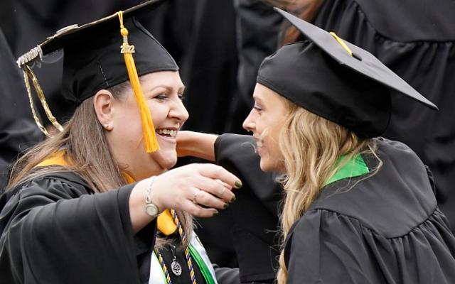 Two graduating students in cap and gown hugging each other