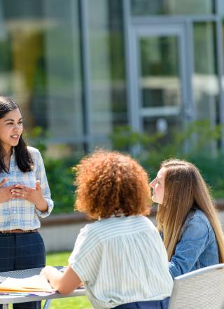 Woman standing on rooftop, speaking to group of three students