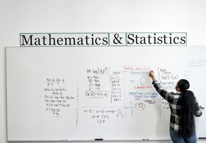 Student writing on whiteboard in Math + Stats lounge