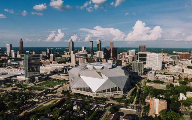 Aerial view of the modern Mercedes-Benz Stadium with the Atlanta city skyline under a blue sky with clouds