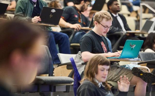 Students sitting in a lecture hall taking notes on laptops during a class at PSU