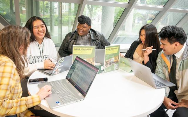 Students gathered around a table with laptops in the PSU School of Business building