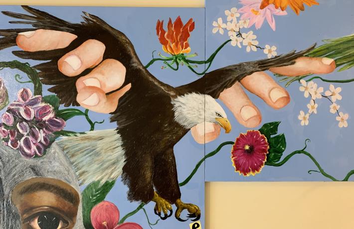 Close-up of an eagle hybrid with human fingers coming out of its wings. It's surrounded by plant life, and the word "free" appears below its feet.