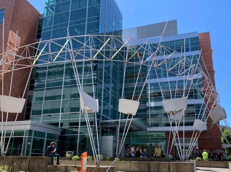 A large metal sculpture stretching over the plaza in front of the Engineering Building, in an arc shape consisting of narrow rods and reflective bars.