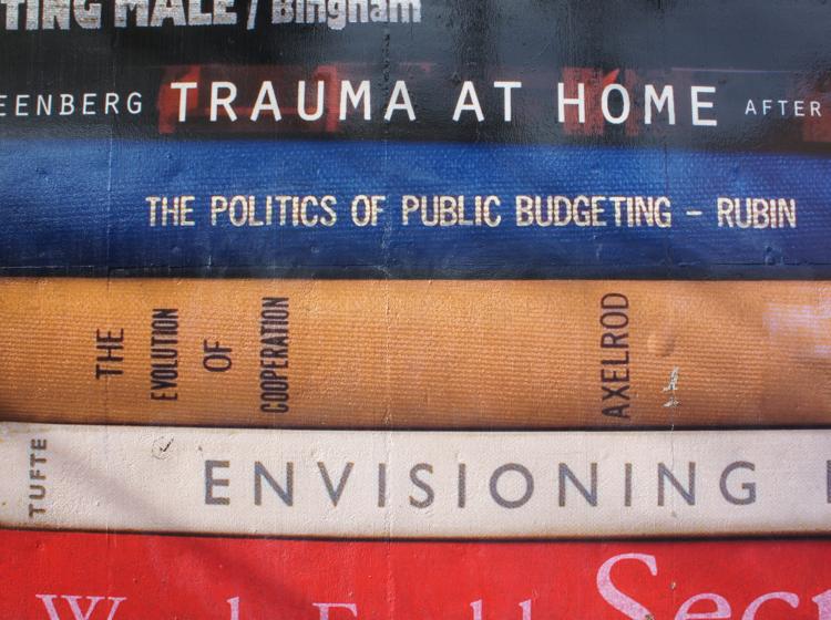 Close-up of the mural. Book titles shown include Trauma At Home, The Politics of Public Budgeting, and The Evolution of Cooperation. 