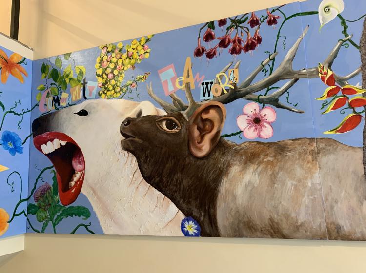 Detail of the mural featuring a deer hybrid and polar bear hybrid. They are surrounded by plant life and the words “community” and “teamwork.”