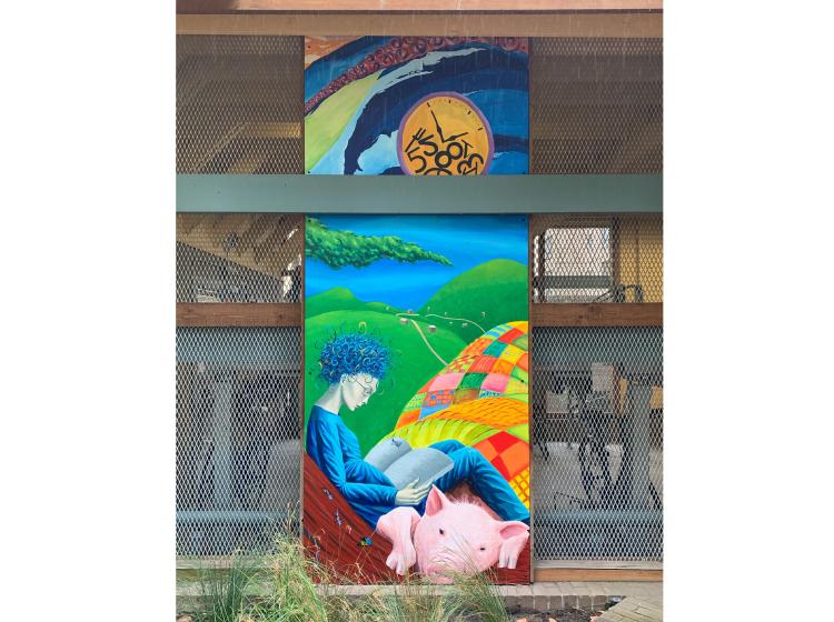 One of three sections of the mural. A tall vertical composition depicts a clock face with numbers scattered randomly, and a woman sitting under a tree reading with a pig.