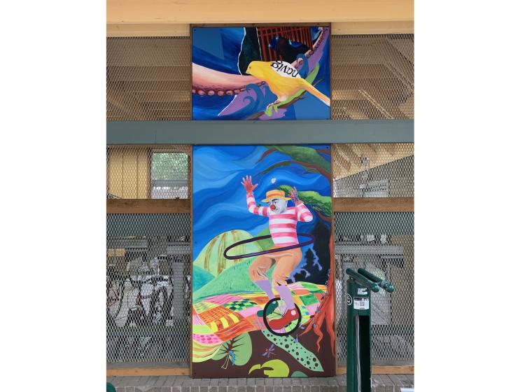 One of three sections of the mural. A tall vertical composition shows a yellow bird with lettering on its back, and a clown riding a unicycle.