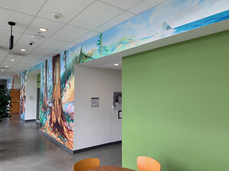 A section of the mural in a hallway. This section of the mural shows Native people stripping wood from a tree.