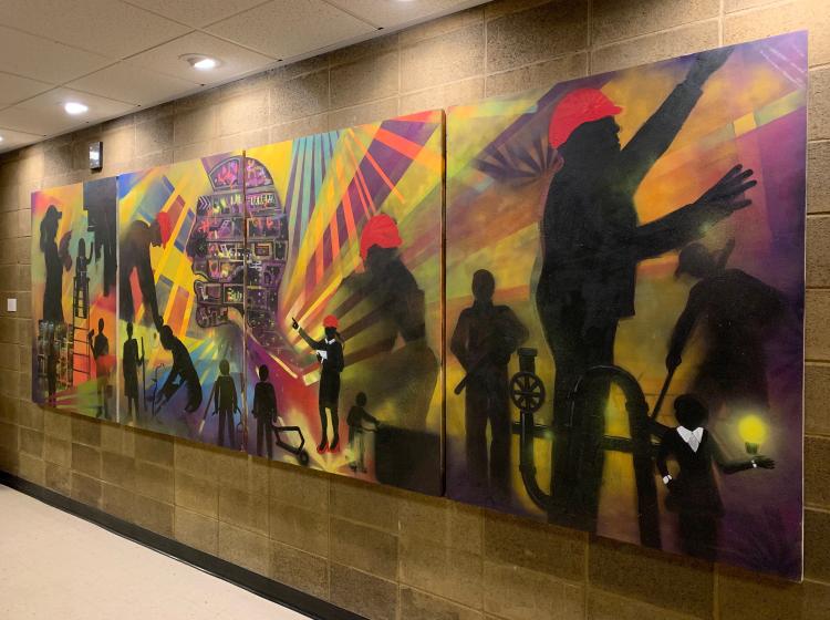 Full mural is shown from the other end. It consists of four panels featuring abstract compositions showing workers with tools.