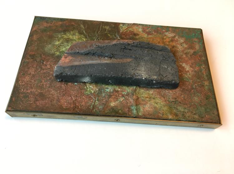 A mixed media artwork against a white background. It includes an abstract sculptural shape on a flat copper panel with brass frame.
