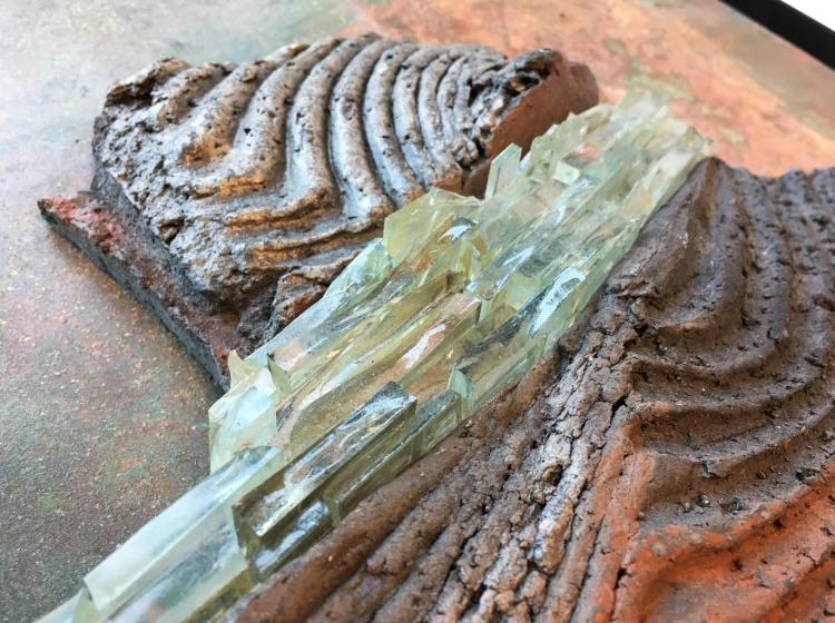 Close-up of an abstract sculptural artwork that includes ceramic ridges around a "river" of glass shards.