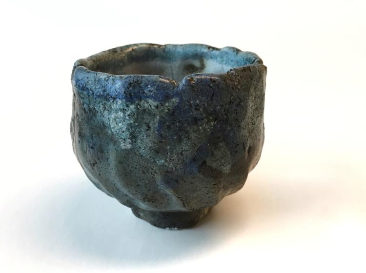 A small ceramic bowl against a white background. It has a slightly irregular, lumpy shape. Its color is a deep celadon green.