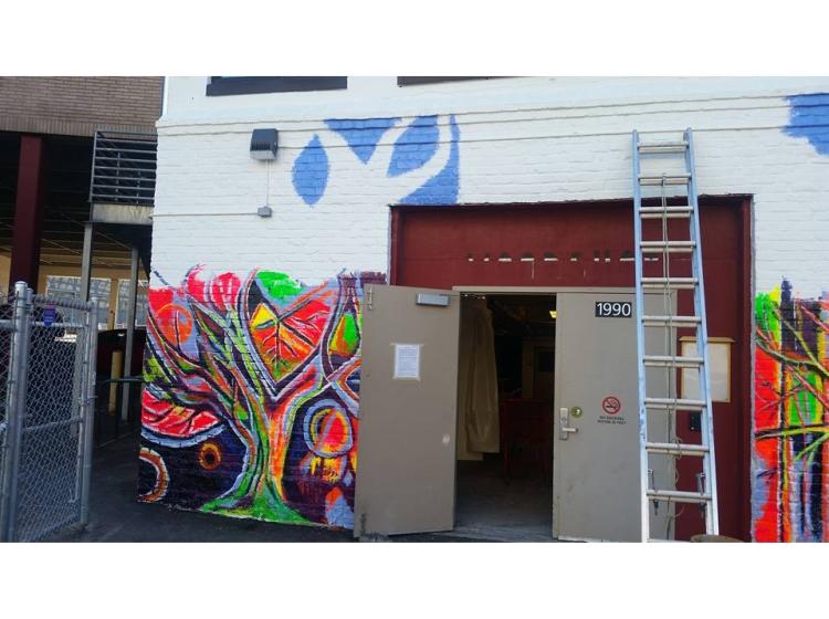 The mural is about halfway finished. The upper half of the wall is white, and the lower half is painted with colorful abstract plant life.