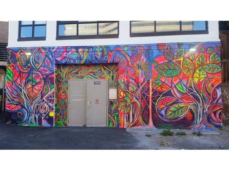 A colorful mural on the exterior wall of a building, an abstract composition of plant life and leaves, in bright greens, pinks and blues.