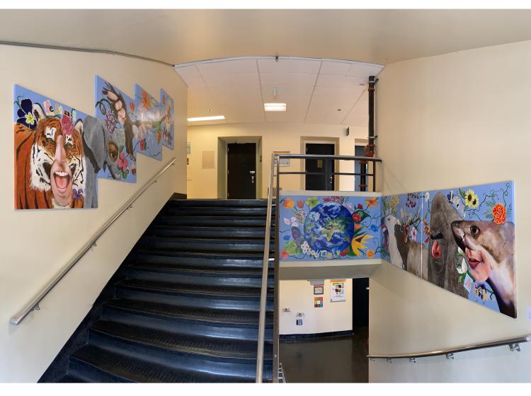 A sectional mural in a stairwell, depicting animal/human hybrids with text such as "be savage" and "be wild and soar.”
