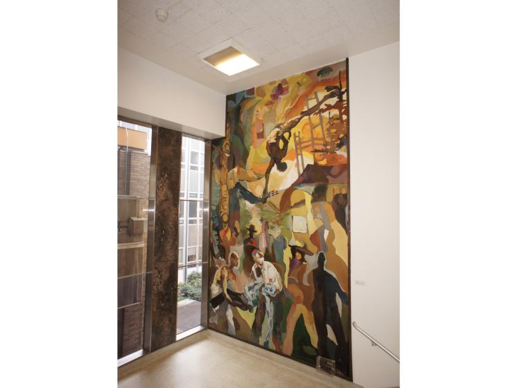 Angled shot of the mural in the stairwell landing, taken from farther back. To the left of the mural are large windows.