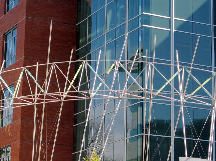 Close-up of a portion of the sculpture, consisting of thin metal rods in an arcing shape that brightly reflect the sunlight. 