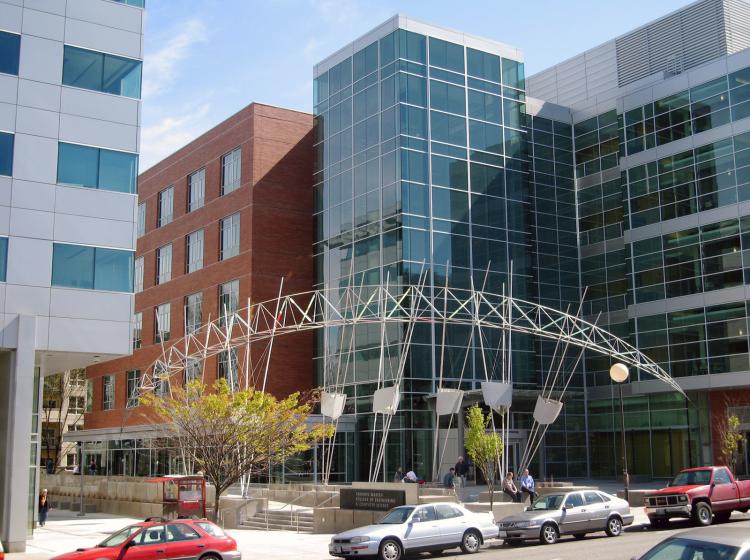 A large sculpture in an arcing shape composed of thin metal rods spans the plaza area in front of the Portland State Engineering Building.