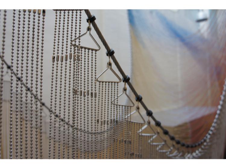 Close-up of hooks and chains that hold up individual strings of colored beads. The hooks are triangular in shape, and each has seven delicate chains hanging from it.