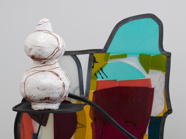 Close-up of the upper portion of the sculpture. A ceramic vessel-like sculpture rests on a shelf that protrudes from the sculpture at left.