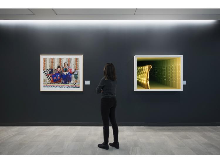 The artwork is seen framed on a dark grey wall, with a person standing and looking at it. Also seen is "Bridge (Rising)" by Glenn Kaino.