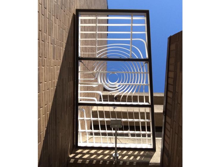A view looking straight up at the smaller, secondary canopy. A bright blue sky can be seen through the flowing grid design.