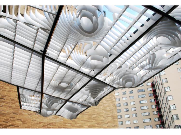 The artwork is seen from underneath. Blue sky is visible through the gaps between a flowing grid of curving white slats.