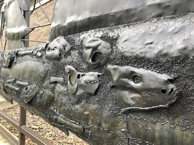 Close-up of a section of the sculpture, depicting dinosaur fossils in the ground