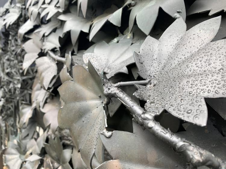 Close-up of a section of the sculpture, depicting leaves and branches. There are raindrops on the metal surface of the sculpture