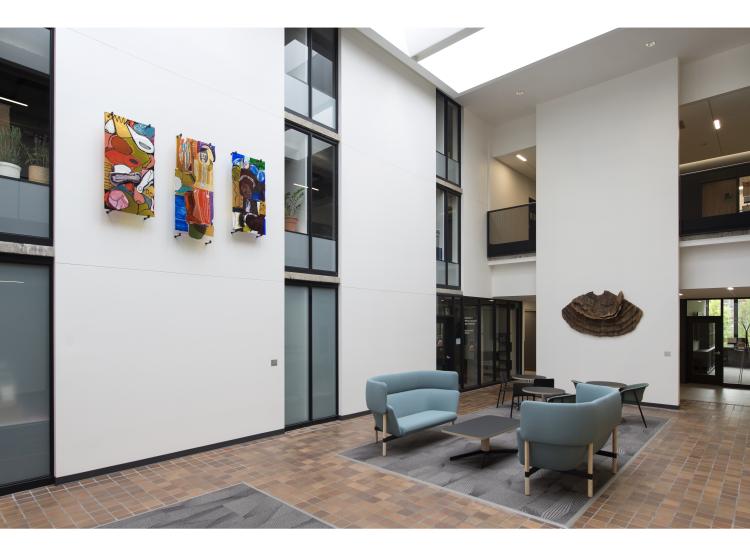 The sculpture is seen mounted on a section of wall, in a wider shot showing the surrounding study lounge in Fariborz Maseeh Hall
